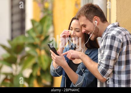 Portrait of a happy couple laughing listening to music online in the street Stock Photo