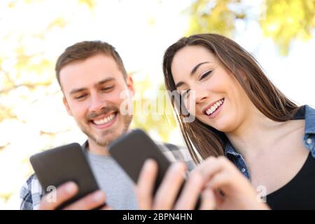 Portrait of a happy couple using their smart phones walking in a park Stock Photo