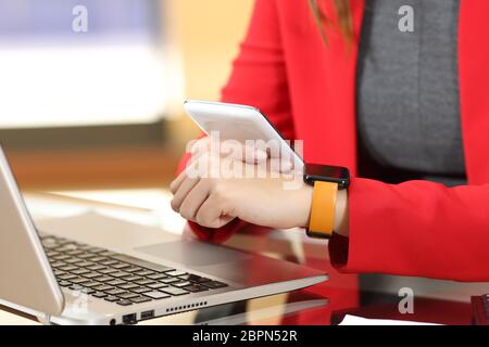 Entrepreneur hands synchronizing smart watch and phone sitting in a desktop at office with her red suit in the background Stock Photo