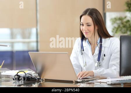 Concentrated doctor working on line with a laptop sitting in a desk in a consultation Stock Photo