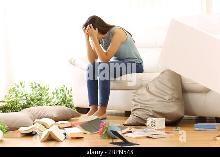 Desperate homeowner complaining after home robbery sitting on a couch of the messy living room at home Stock Photo