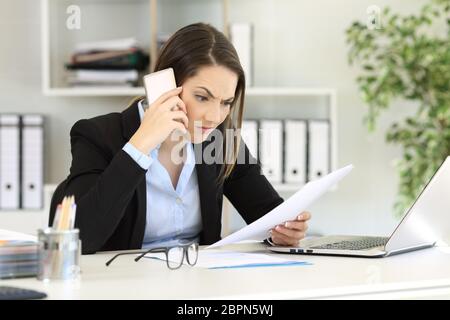 Angry executive calling on phone reading a paper document at office Stock Photo