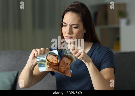 Angry girl breaking a couple photo after breakup sitting on a couch in the living room at home Stock Photo