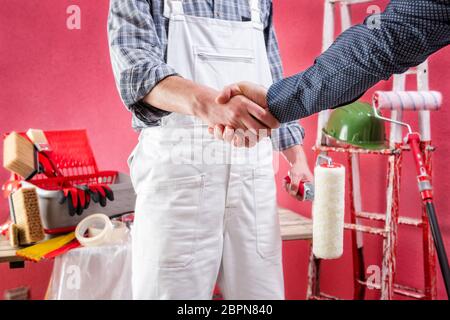 Young Caucasian house painter worker in white work overalls shake hands. Construction industry. Work safety. Stock Photo