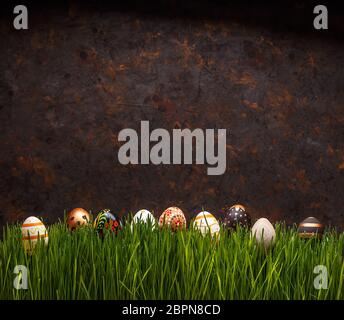 Row of Easter eggs hiding in grass on grungy dark background, copy space Stock Photo