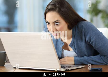 Perplexed woman reading online news in a laptop on a desk at home Stock Photo