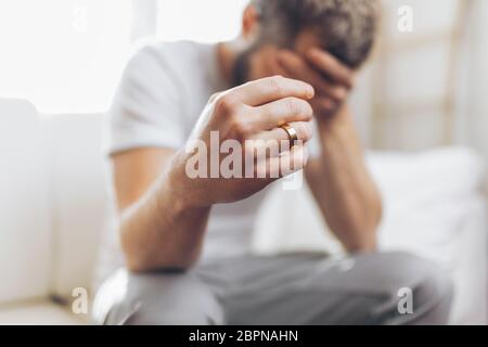 Heartbroken man at home holding a wedding ring Stock Photo