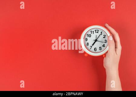 The alarm clock is set for 7 am. A woman's hand holds a watch on a red background Stock Photo