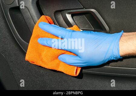 Hand of driver in blue protective glove is wiping with a cloth an interior handle of car door. Coronavirus or Covid-19 car disinfection Stock Photo