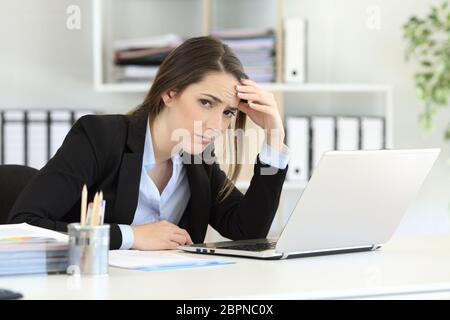 Worried office worker looking at camera sitting in a desktop Stock Photo
