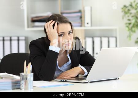 Worried office worker looking at camera sitting in a desk at workplace Stock Photo