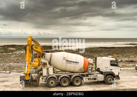 PORTHCAWL, WALES - JUNE 2018: Concrete mixer unloading ready mixed concrete into the bucket of a heavy duty excavator to strength sea defences Stock Photo