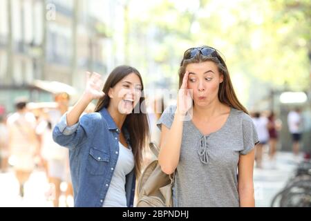 Happy teen greeting waving hand and friend ignoring her in the street Stock Photo