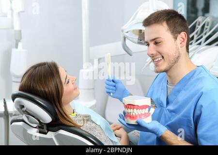 Happy dentist explaining teeth brushing procedure to a patient in a office Stock Photo