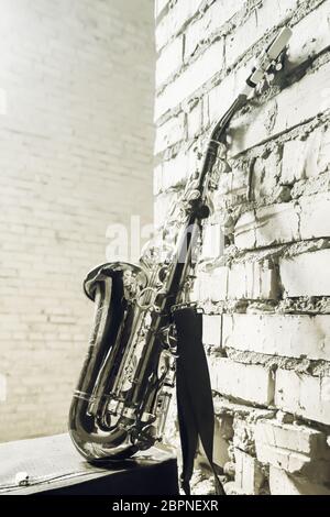 Musical woodwind instrument saxophone with old briefcase on the brick wall background. Vintage stylized monochrome toned concept image with space for Stock Photo