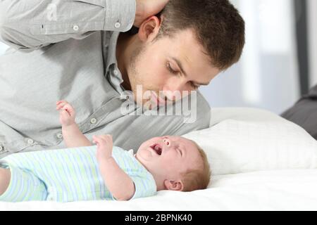 Confused father watching his baby son crying desperately on a bed Stock Photo