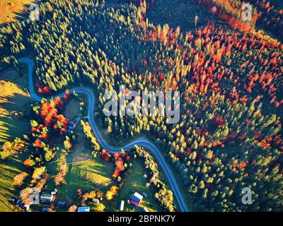 Curved road trough fall forest and village. High mountain pass in Carpathian mountains, Ukraine. Autumn top aerial view from drone. Stock Photo