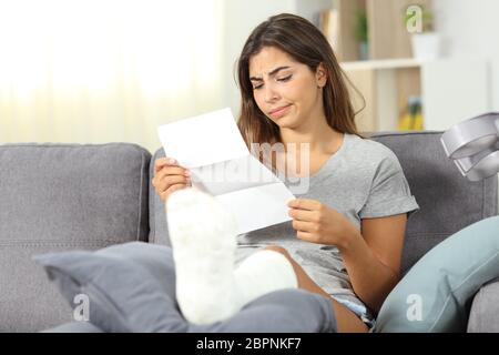 Disoppointed disabled woman reading a letter sitting on a couch in the living room at home Stock Photo
