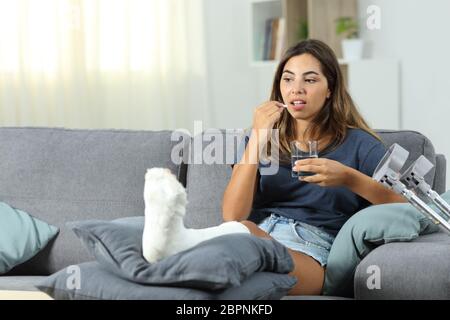Disabled woman taking a painkiller pill sitting on a couch in the living room at home Stock Photo