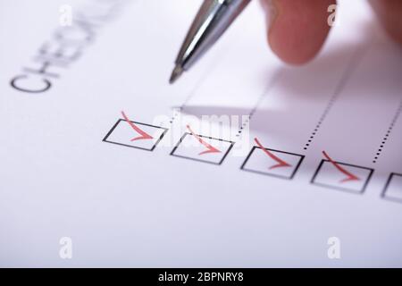 Close-up Of Person's Hand Marking On Checklist With Pen Stock Photo