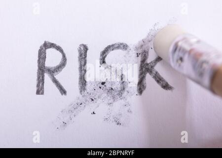 Close-up Of Pencil Eraser Erasing Risk Text On White Paper Stock Photo