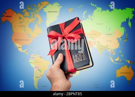 Hand giving the Holy Bible gift against world map. Stock Photo