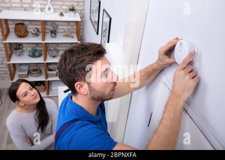Pretty Woman Standing Near Repairman Installing Smoke Detector On Wall At Home Stock Photo