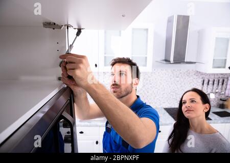 Woman Looking At Male Handyman Installing Cabinet Door In The Kitchen Stock Photo