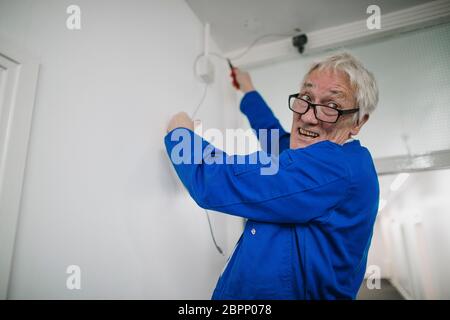 Senior electrician is fitting a security camera system in an office corridor. Stock Photo
