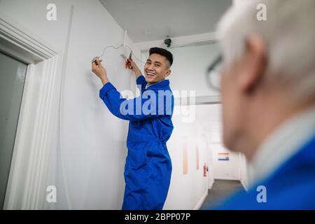 Trainee electrician is fitting a security camera with assistance from his tutor. Stock Photo