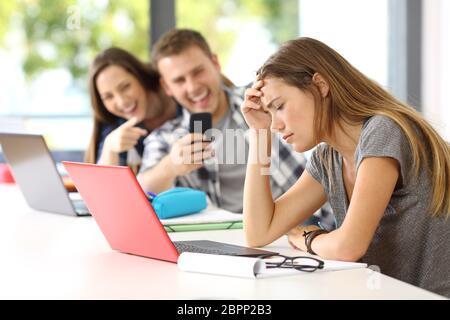 Sad student victim of cyber bullying sitting in a desk in a classroom Stock Photo