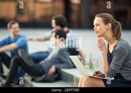 Portrait of a sleek young woman, using laptop computer, being pensive in urban/city context (shallow DOF; color toned image) Stock Photo