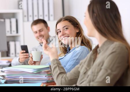 POrtrait of three lazy employees talking and wasting time sitting on a desk at office Stock Photo