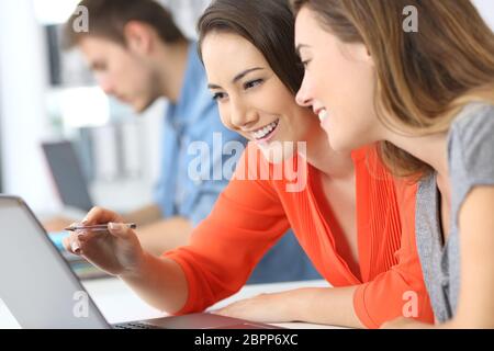 Two employees co-working on line with a laptop at office Stock Photo