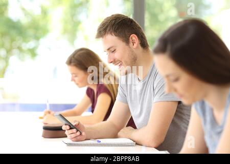 Side view of a student distracted with a mobile phone during a class at classroom Stock Photo