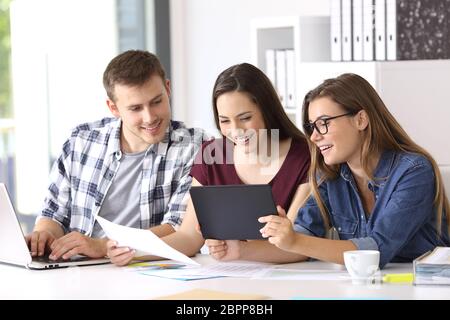 Three happy employees working on line with a tablet and documents at office Stock Photo