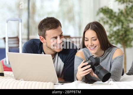 Couple of tourists watching photos from a digital camera and downloading to a laptop on the bed of an hotel room in vacations Stock Photo
