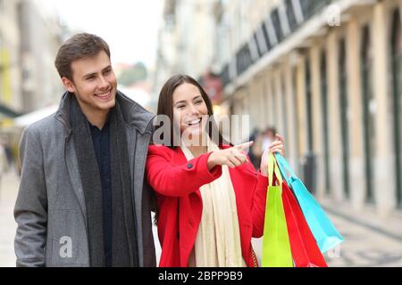 Happy couple shopping pointing at stores walking in an old town street Stock Photo