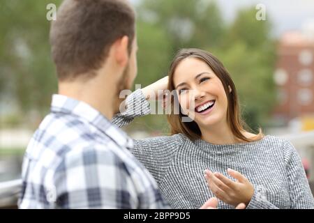 Happy casual couple talking looking each other sitting in a balcony with a green urban background Stock Photo