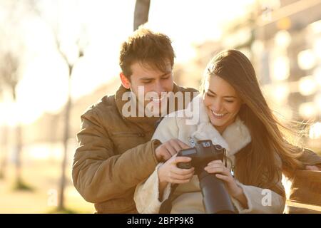 Happy couple checking photos on a dslr camera sitting on a bench in a park Stock Photo