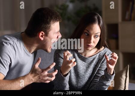 Couple arguing and shouting sitting on a couch in the living room at home with a dark background Stock Photo