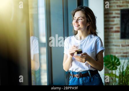 Young pretty woman drinking morning coffee near windows at home Stock Photo