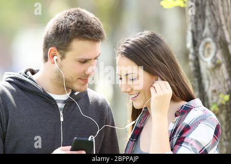 Couple flirting and sharing music on line with earphones and a smart phone outdoors in a park Stock Photo