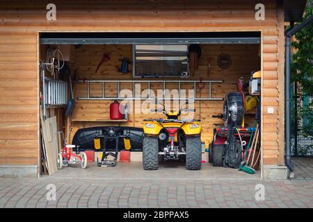 Facade front view open door ATV quad bike motorcycle parking messy garage building with wooden siding at home driveway backyard and lawn path. House Stock Photo