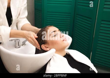 Beautiful young girl washes her head in a beauty studio. Hairdresser is washing hair for client Stock Photo