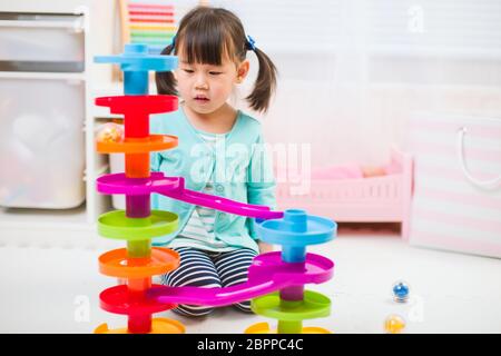 toddler girl play marble run game at home against white background Stock Photo