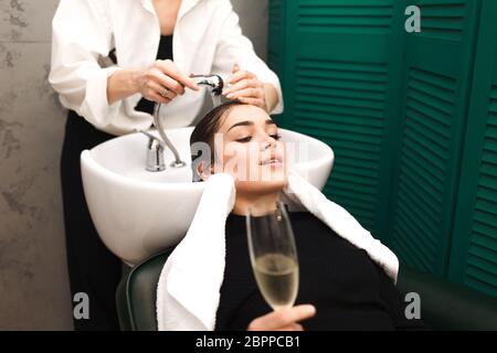 Young girl relaxes in a beauty salon with a glass of champagne while washing hair Stock Photo