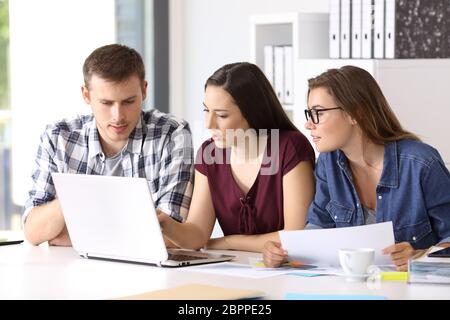 Three entrepreneurs coworking on line with a laptop sitting in a desktop at office Stock Photo