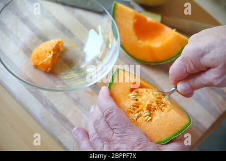 Older man scoops cantaloupe seeds with spoon Stock Photo