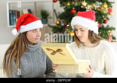 Disappointed woman receiving a gift from a frustrated friend in christmas at home Stock Photo